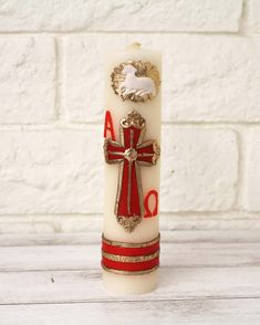 a white candle with red and gold trimmings on it sitting next to a brick wall