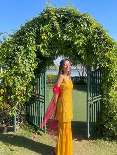 a woman in a yellow dress is standing under a green arch with flowers on it