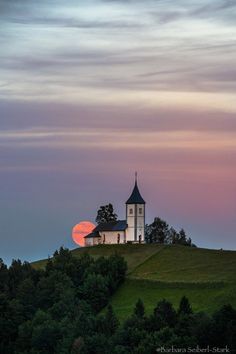 a church on top of a hill with the sun setting in the distance behind it