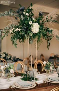 a tall centerpiece with white flowers and greenery sits on top of a table