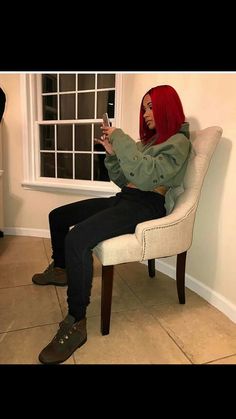 a woman sitting in a chair looking at her cell phone while wearing a red head scarf