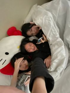 three women laying in bed with a hello kitty pillow