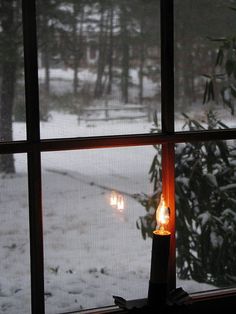 a lit candle sitting on top of a window sill in front of snow covered ground