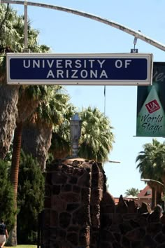 a street sign hanging from the side of a metal pole near palm trees and buildings