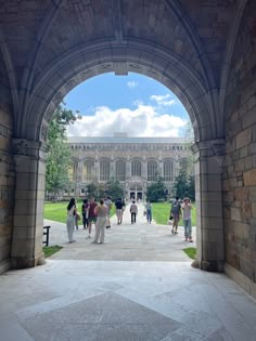 a group of people walking under an arch on a walkway in front of a building