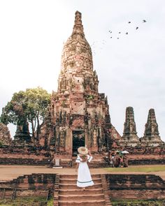 a woman in a white dress and straw hat standing at the entrance to an ancient temple