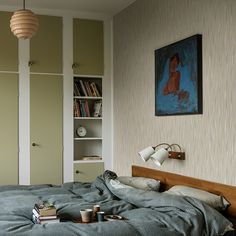 an unmade bed in a bedroom with books on the floor and a painting hanging above it