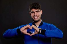 a young man is making a heart shape with his hands and smiling at the camera