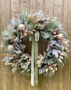 a christmas wreath with pine cones and greenery hanging on a wooden wall next to a fence