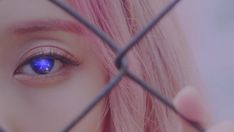 a woman with pink hair and blue eyes looking through a fence