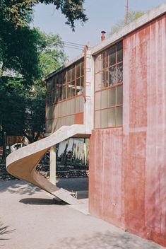 an upside down slide in front of a red building with windows on the side and trees behind it