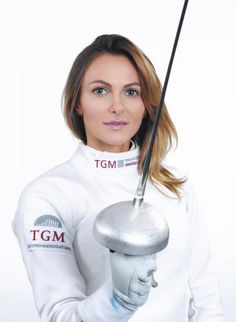 a woman holding a golf club in her right hand and wearing a white jacket with the words tgm on it