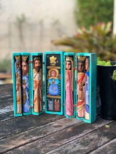 four wooden nativity figurines sitting on a table next to a potted plant