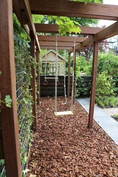 a swing set in the middle of a garden with leaves on the ground and trees around it