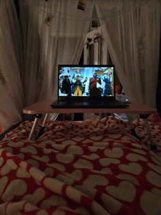 a laptop computer sitting on top of a bed in front of a tv screen and curtains