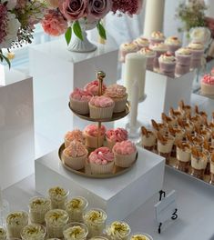 three tiered cupcake display with pink flowers and other desserts on the table