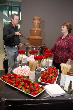 a man and woman standing in front of a chocolate fountain with strawberries on it