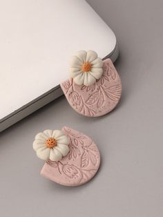 two pink and white flower shaped earrings on top of a laptop computer keyboard next to it