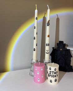 three candles sitting next to each other on top of a table with a rainbow in the background