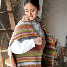 a woman wearing a multicolored shawl standing in front of a wooden ladder