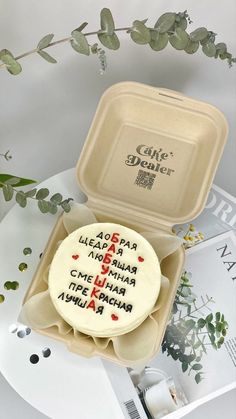 a cake in a box with writing on it and some flowers next to the package