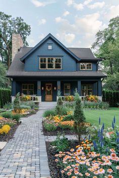 a blue house with lots of flowers in the front yard and walkway leading to it