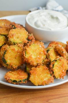 some fried food on a white plate next to a small bowl of ranch dips