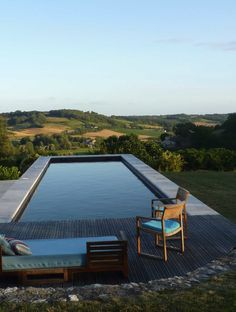 an empty swimming pool surrounded by wooden decking and lawn furniture with chairs around it