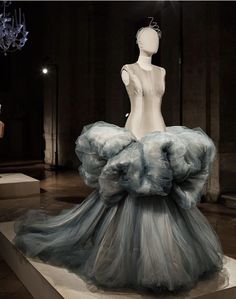 a dress on display in a museum with chandeliers hanging from the ceiling behind it