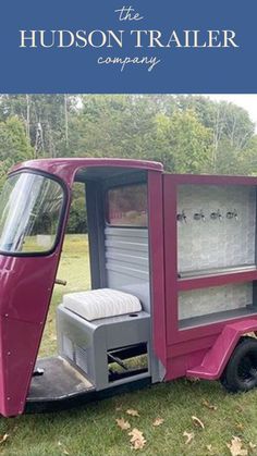 a pink truck parked on top of a lush green field with trees in the background