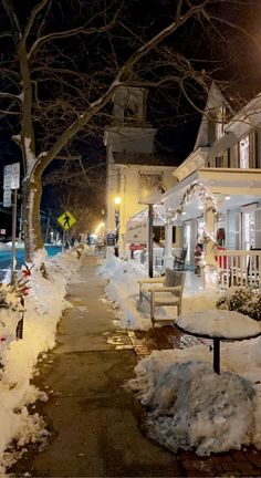 a snowy sidewalk with snow covered benches and tables on it at night in front of a building