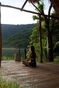 a woman sitting on a wooden deck in front of a body of water and trees