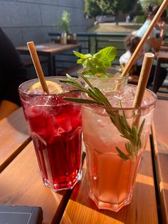 two glasses filled with drinks sitting on top of a wooden table next to each other