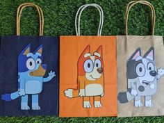 three bags with cartoon characters on them sitting in the grass, one is blue and one is orange