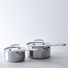 two stainless steel pots and pans sitting on a table with white wall in the background