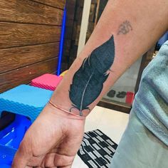 a person with a tattoo on their arm holding a black feather in one hand and an arrow in the other