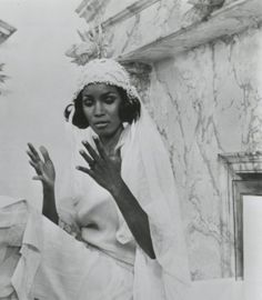 a black and white photo of a woman wearing a headdress with her hands in the air