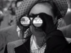 black and white photograph of woman with sun glasses looking through binoculars at other people in the background