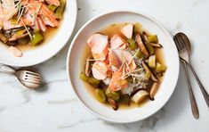 two white bowls filled with food on top of a table next to utensils