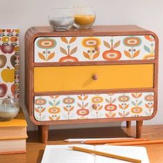 an orange and yellow painted dresser next to some books on a wooden table with two glasses