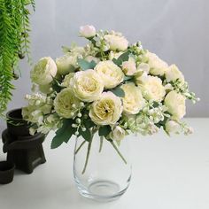 a vase filled with white flowers sitting on top of a table next to a plant