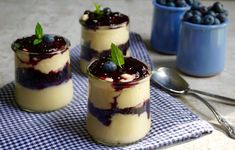 three small desserts with blueberries and cream in them on a napkin next to spoons