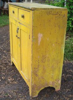 an old yellow cabinet sitting on top of a gravel ground next to grass and bushes