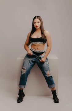 a woman sitting on top of a white block wearing ripped jeans and cropped tank top