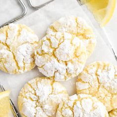 lemon crinkle cookies with powdered sugar are on a cooling rack next to a lemon wedge