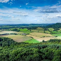 an aerial view of the countryside with many trees and fields in the foreground, on a sunny day