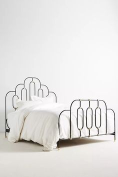 an iron bed frame with white linens and gold accents on the headboard is shown in front of a plain white wall