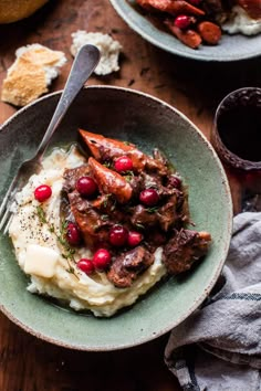 two bowls filled with mashed potatoes and meat on top of a wooden table next to a glass of wine