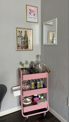 a pink cart filled with lots of bottles next to a mirror and pictures on the wall