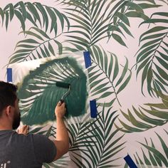 a man painting a wall with palm leaves on it and blue tape around the edges